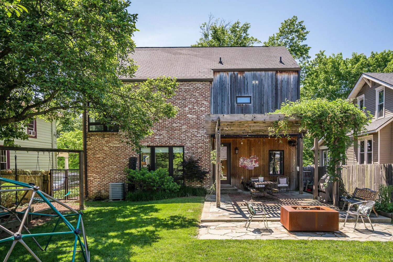 A serene backyard of a custom built home with a brick exterior, a rustic patio, and a vine-covered pergola, a perfect setting for outdoor living.