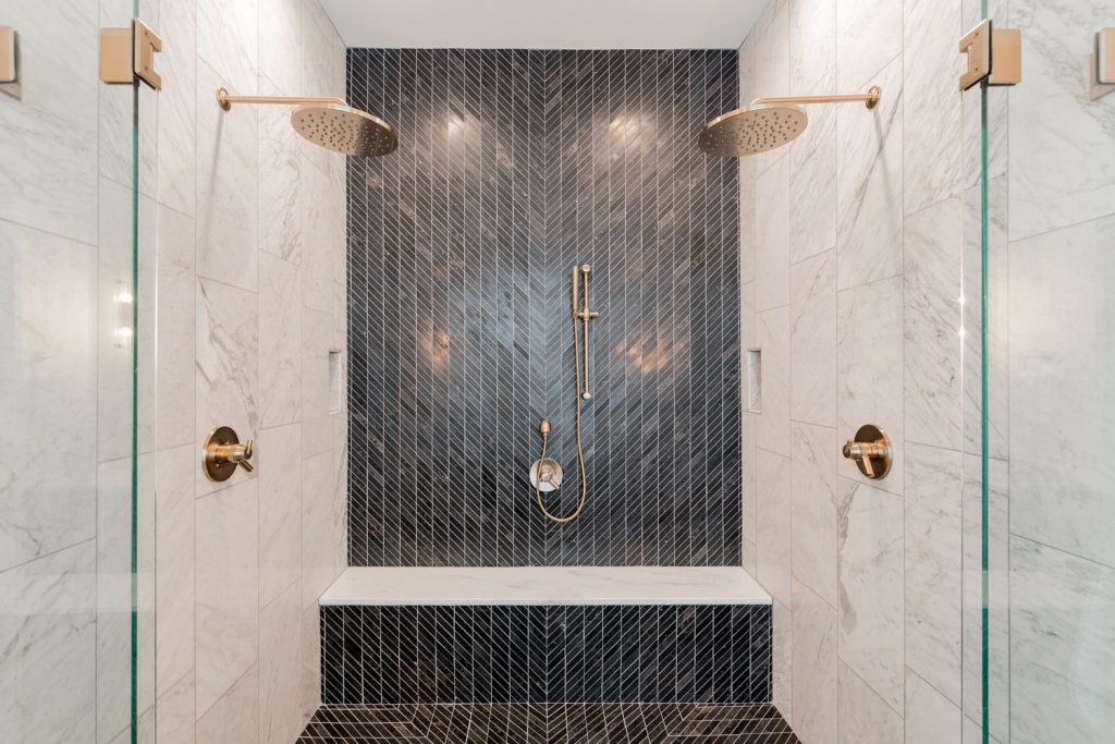 Elegant Louisville shower by luxury custom home builders featuring gold fixtures and black-and-white marble walls.