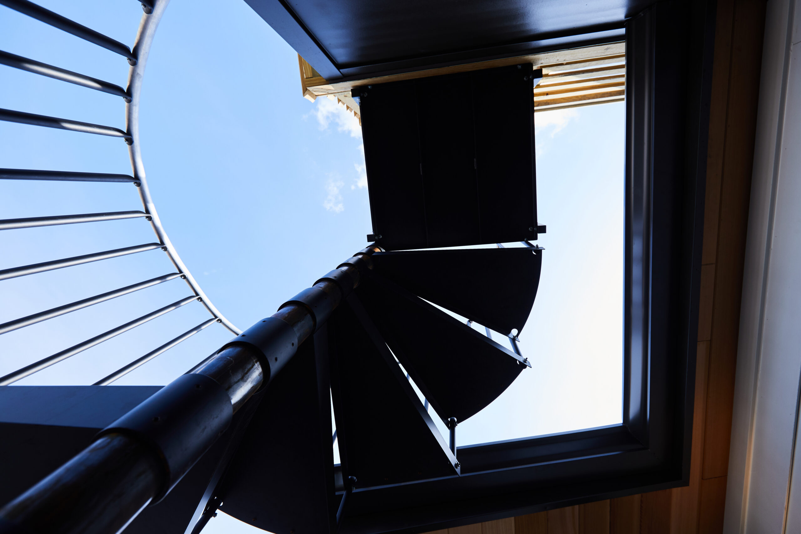 A dramatic view from below a black spiral staircase, highlighting the unique design and artistry of a custom built home.