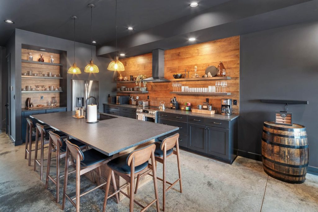 Louisville modern kitchen with dark cabinets, wooden backsplash, large island, stools, pendant lights, and open shelves.