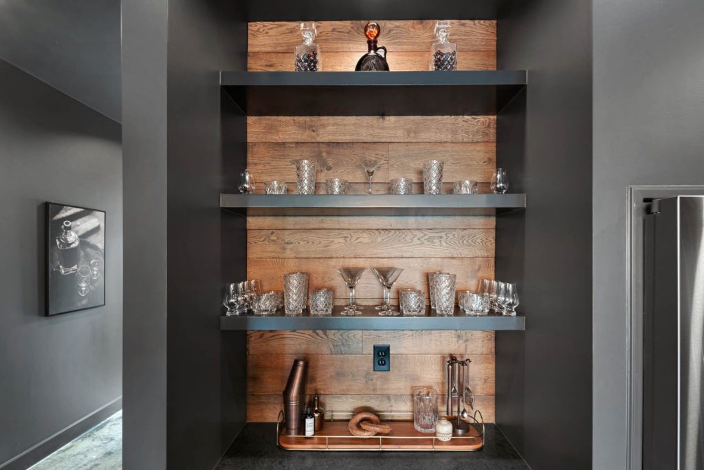 Louisville modern home bar with wooden panel shelves, crystal glassware, decanters, and cocktail tools on a tray.