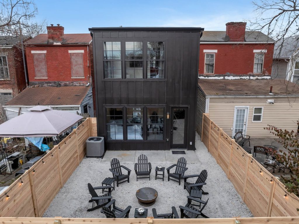 Louisville modern farmhouse with black exterior, large windows, circular fire pit, Adirondack chairs, and private wooden fence.