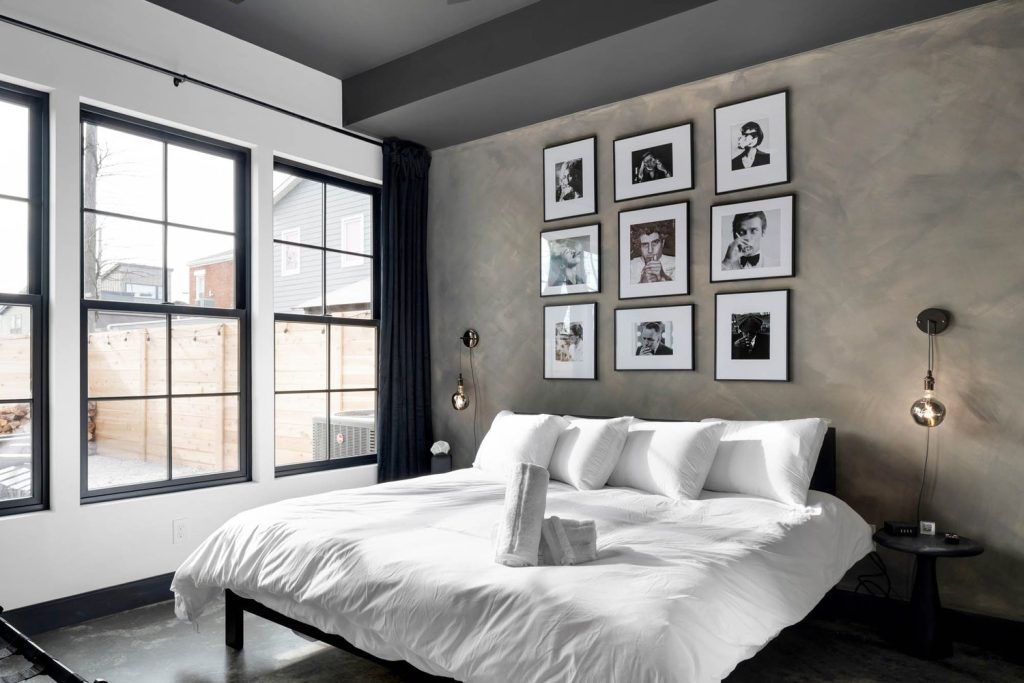 Louisville modern bedroom with white bed, gray accent wall, black-and-white art, large windows, and stylish lighting.