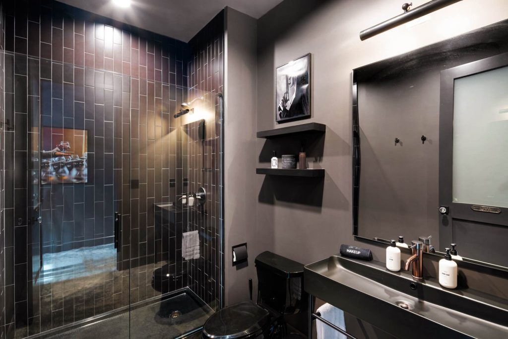 Louisville modern bathroom with dark tiles, glass shower, black fixtures, wall shelves, and stylish minimalist design.