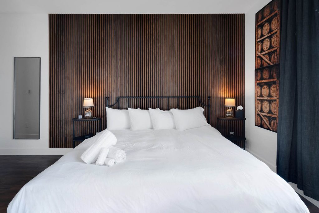 Louisville cozy bedroom with white bed, matching nightstands, and textured wood accent wall showcasing refined custom home design ideas.
