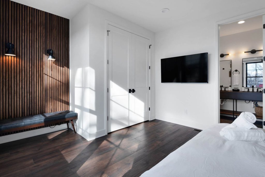 Louisville minimalist bedroom with dark wood floors, slatted accent wall, wall-mounted TV, and custom home design details.