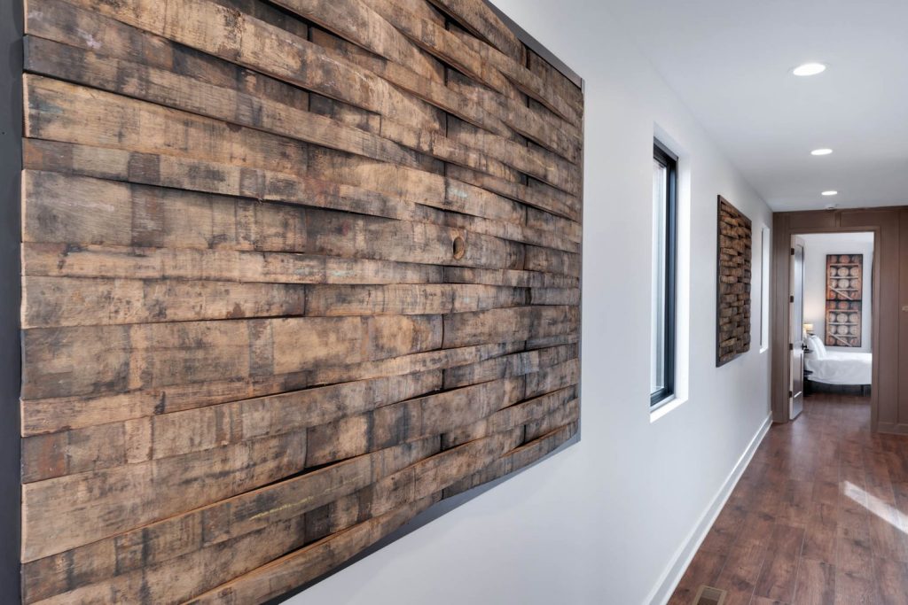 Modern hallway with abstract wooden wall art featuring natural textures and geometric patterns, softly lit by a window for a serene custom home design feel.