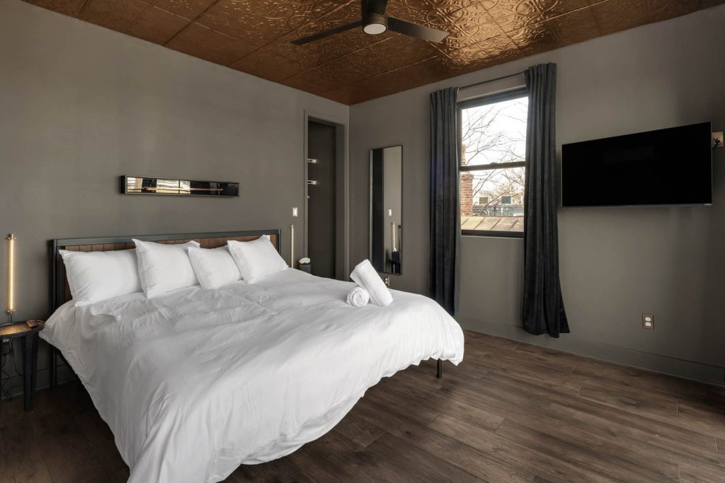 Minimalist modern bedroom with white bed, dark curtains, wooden floor, and gold ceiling. Calm, inviting ambiance.