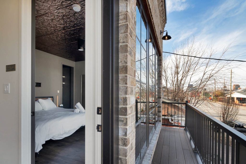 Cozy modern bedroom with white bedding, rustic balcony, and cityscape view. Serene winter ambiance with natural light.