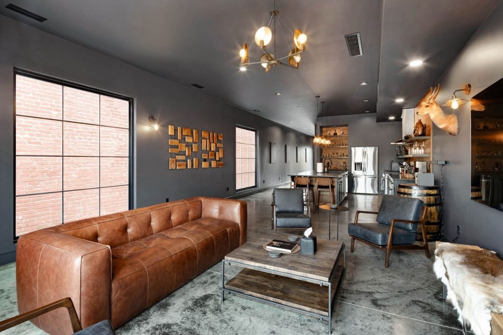 Louisville modern industrial living room with brown leather sofa, blue chairs, large windows, and open kitchen.