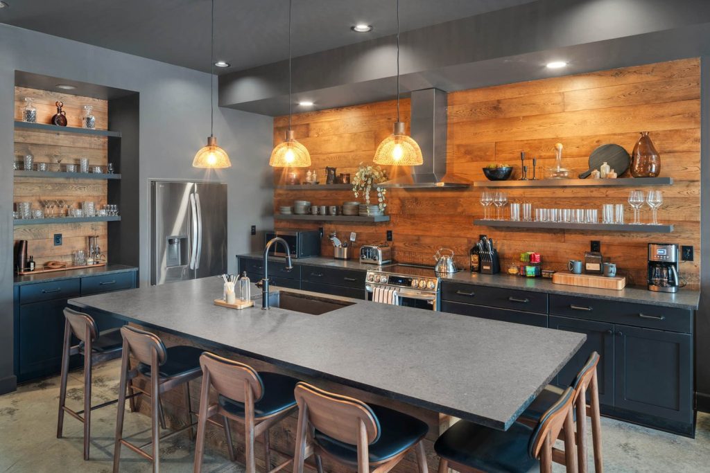 Louisville modern kitchen with gray island, wooden bar stools, warm wood backsplash, and hanging pendant lights.