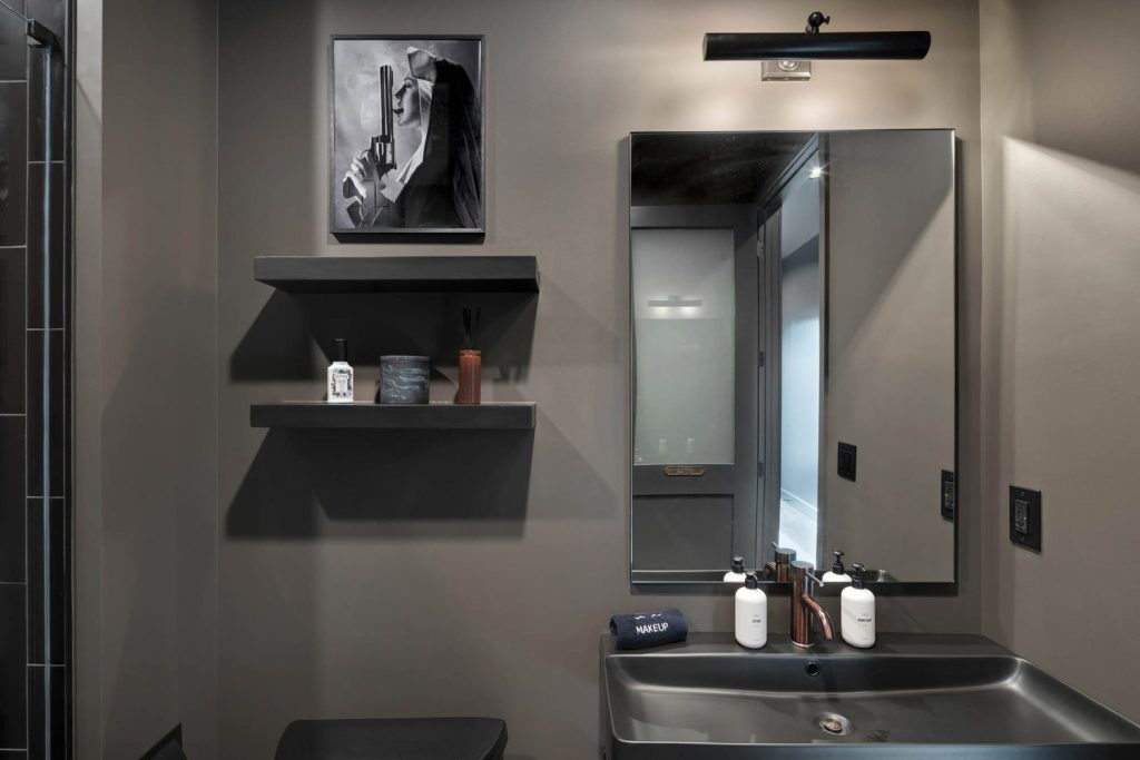 Louisville modern bathroom with gray walls, black sink and mirror, shelves with toiletries, and unique artwork.