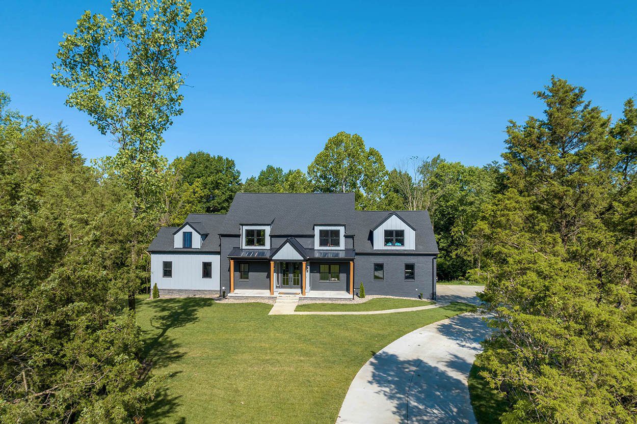 Black and white home with a striking triangular roof, curved driveway, and lush landscaping, highlighting bold new construction design.