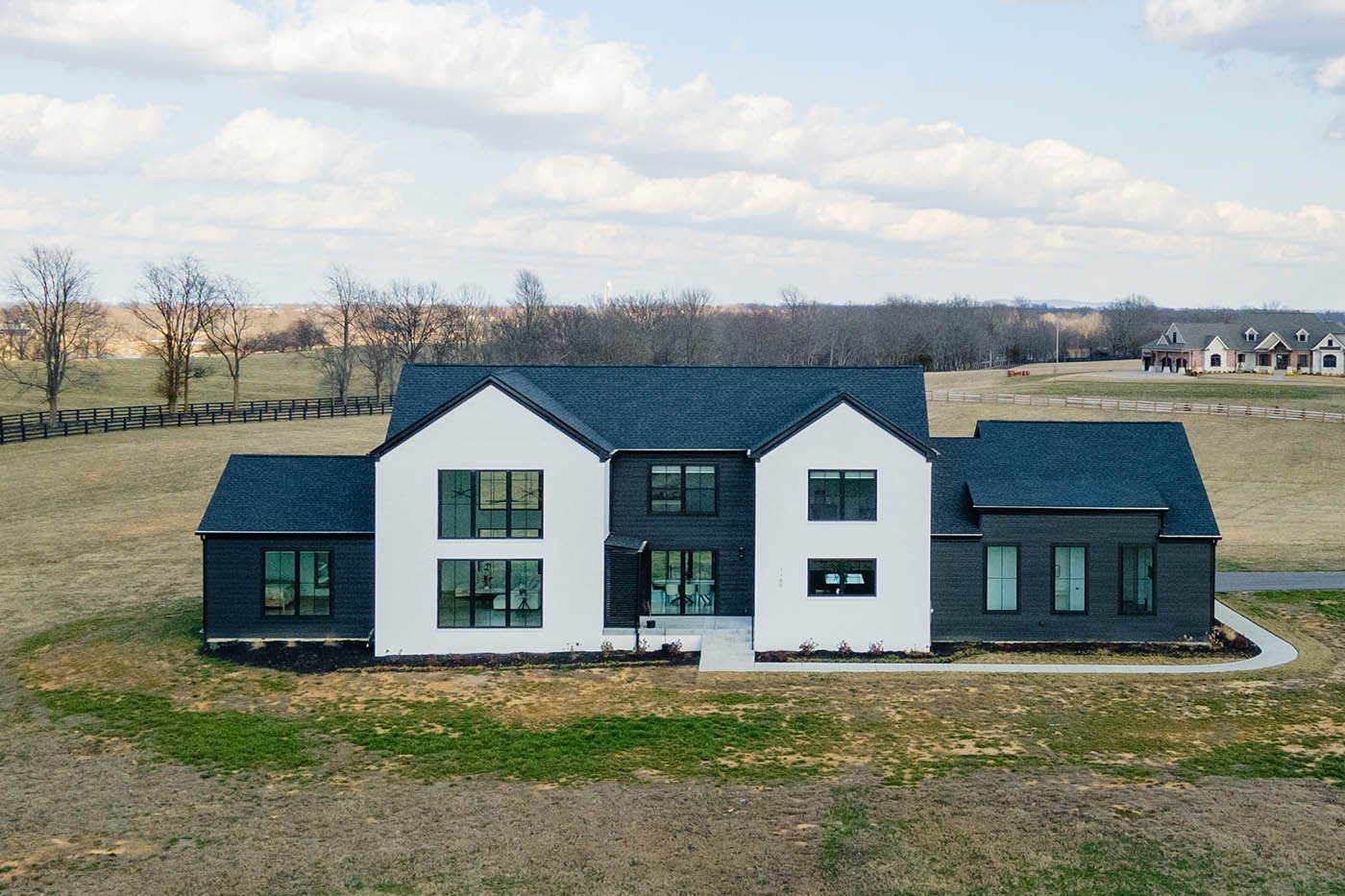 Louisville modern farmhouse with white and charcoal exterior, large windows, and open fields by top custom home builders.