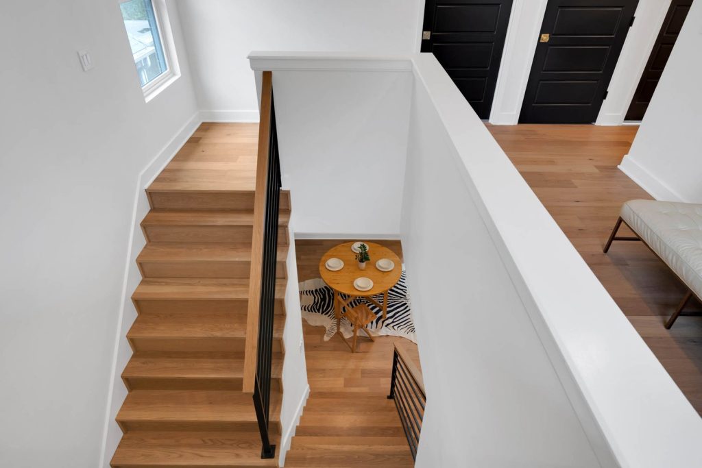 Overhead view of a wood staircase leading to a round dining table on a zebra rug, framed by black doors and clean lines.