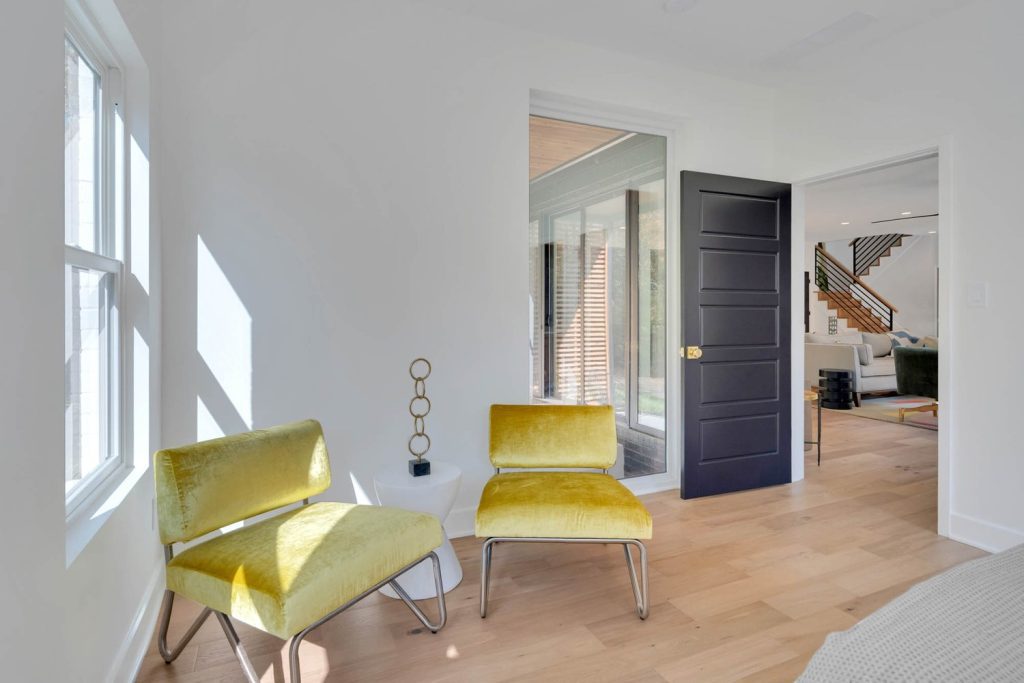 Spacious living area with yellow velvet chairs, geometric table sculpture, and sunlight streaming through large windows.