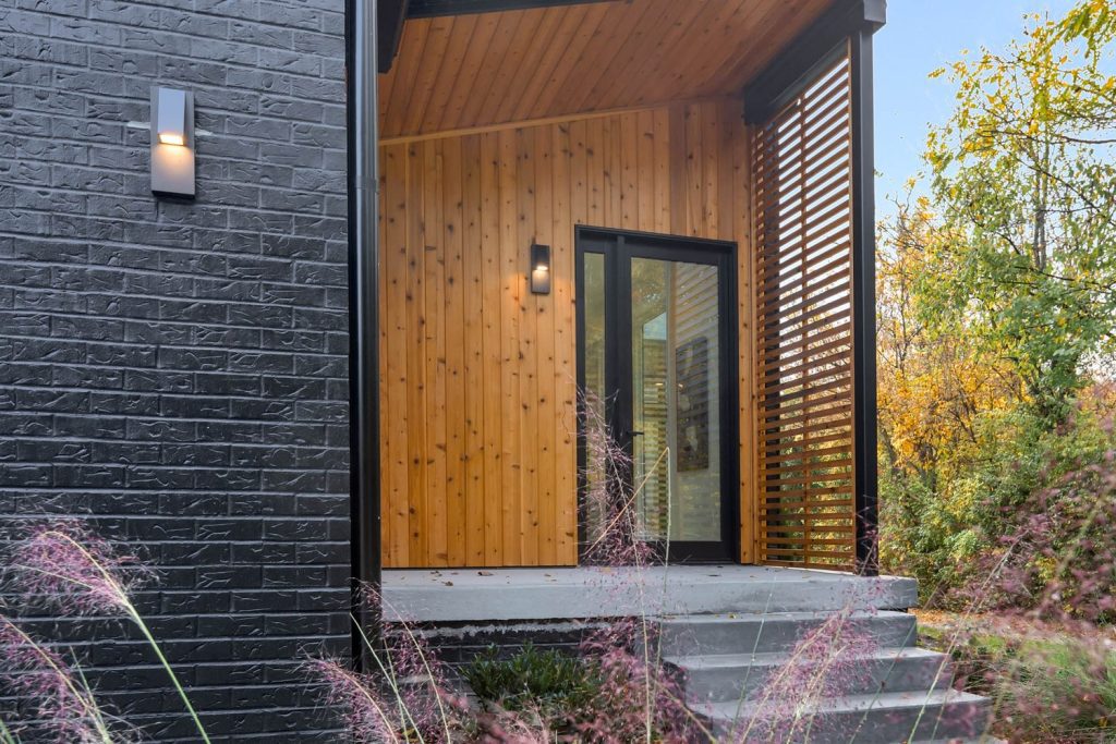 Modern house entrance with black brick, warm wood paneling, and glass door. Minimalist, serene, inviting design.