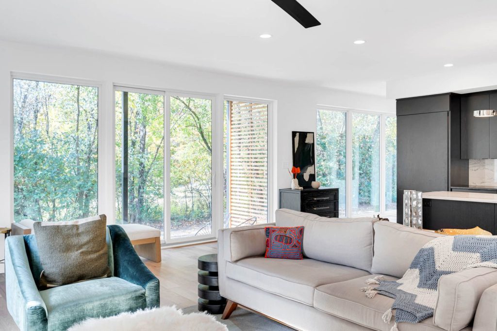 Modern living room with white sofa, green chair, and large windows overlooking a lush garden in a bright new construction home.