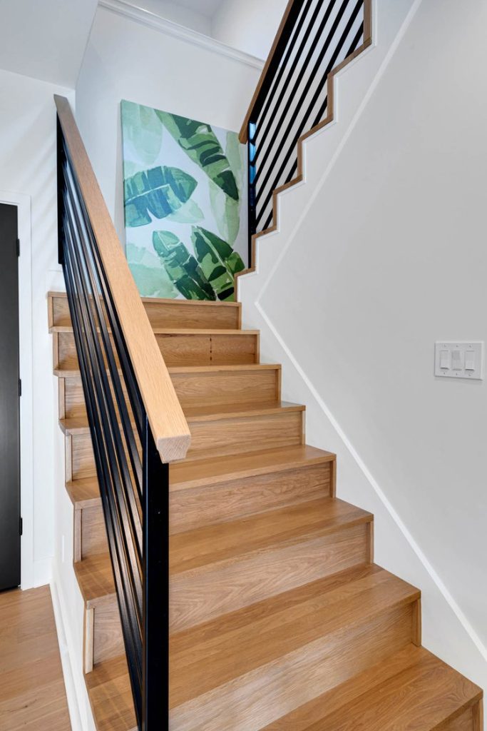 Wooden staircase with black metal railing and green banana leaf wallpaper. Fresh, contemporary style with natural accents.