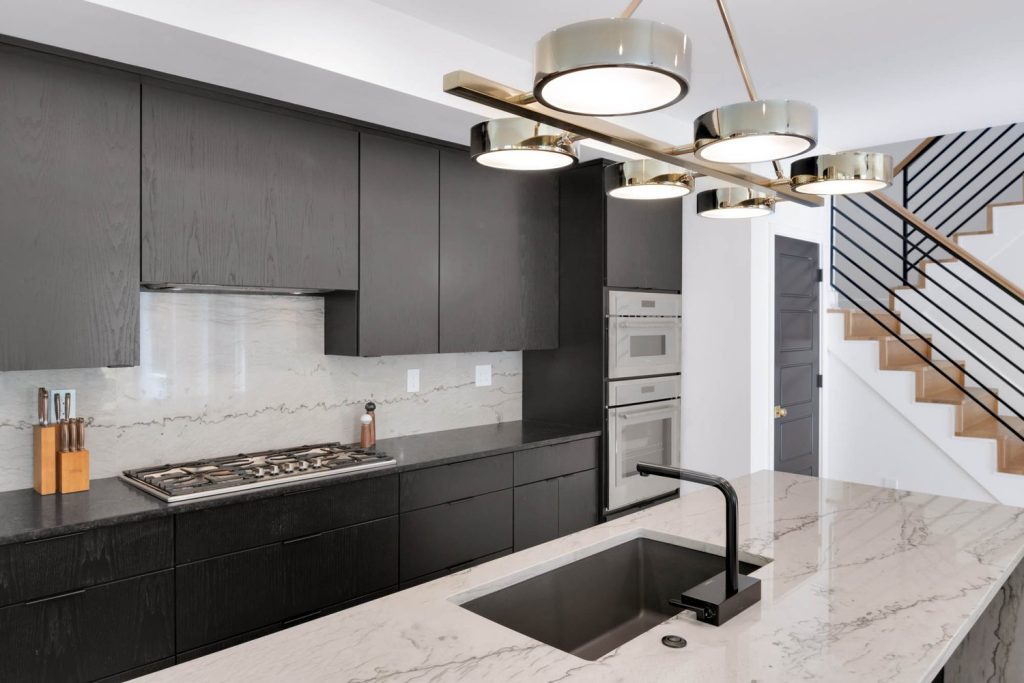 Modern kitchen with dark cabinets, marble counters, black sink, and round pendant lights for a sleek, elegant look.
