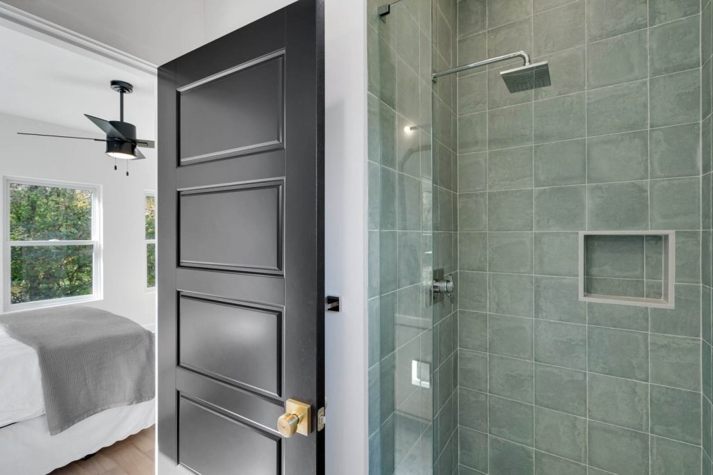 Black door opens to a bathroom with a glass shower, gray tiles, and minimalist design, creating a crisp, clean look.