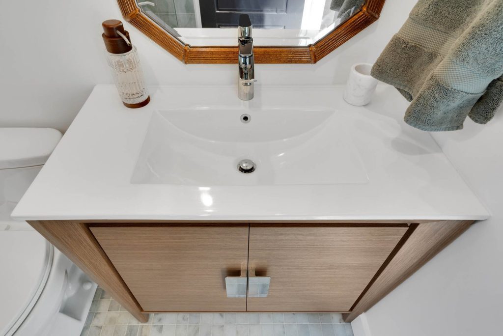 Wood vanity with dual doors and a sleek sink, octagonal mirror, and subtle décor creating a tidy, minimalist bathroom setting.
