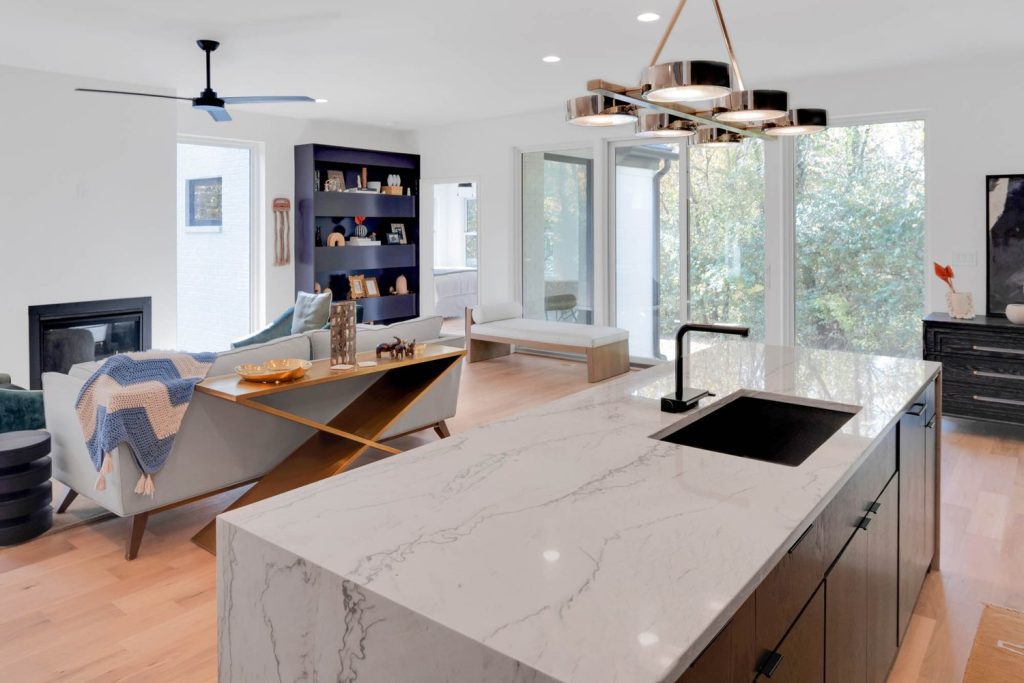 Modern kitchen with matte black cabinets, marble island, brass pendant lights, under-mount sink, and bright natural light.