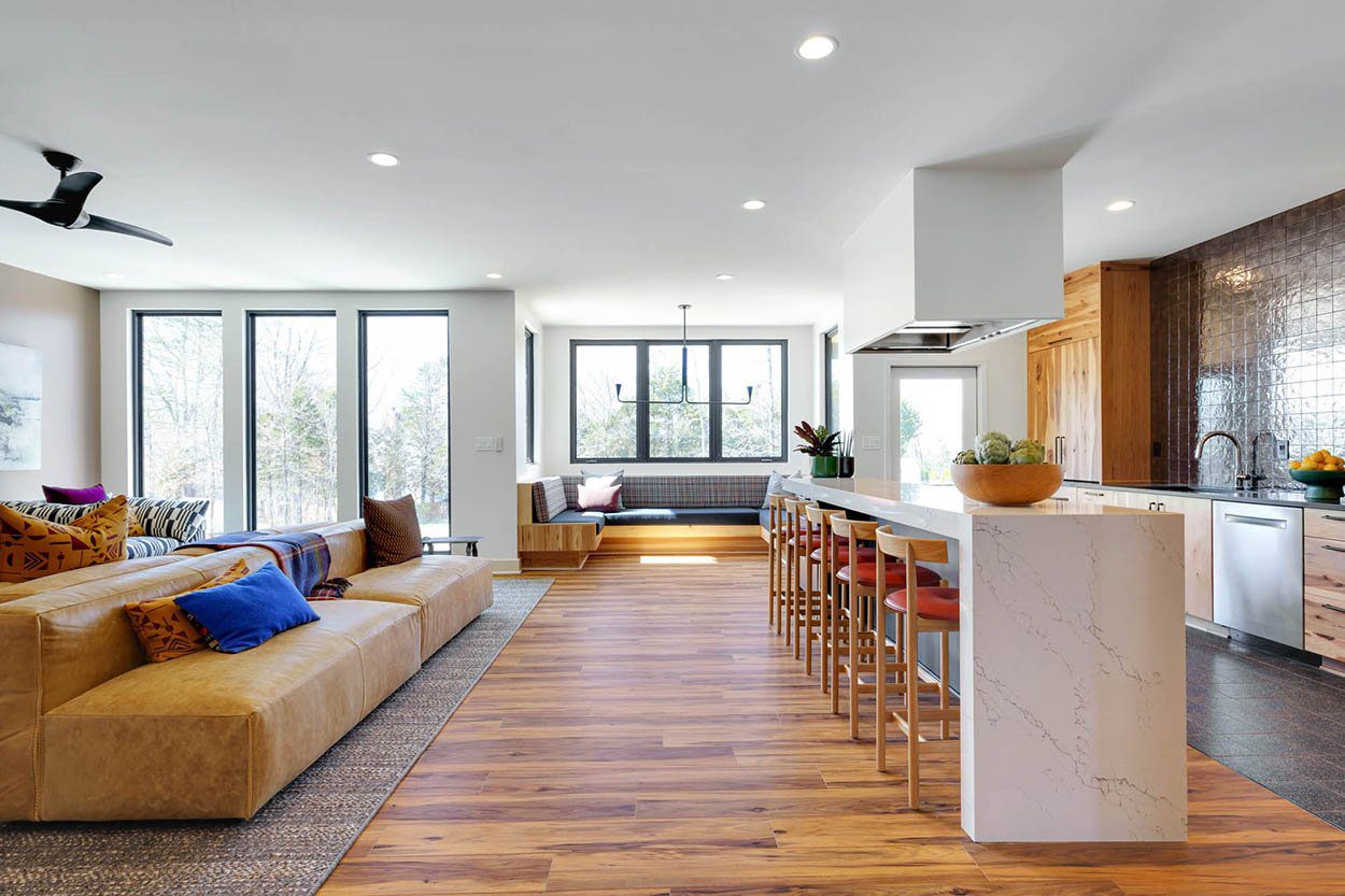 Modern open-concept living space with tan sectional, colorful pillows, and marble kitchen island with wood stools