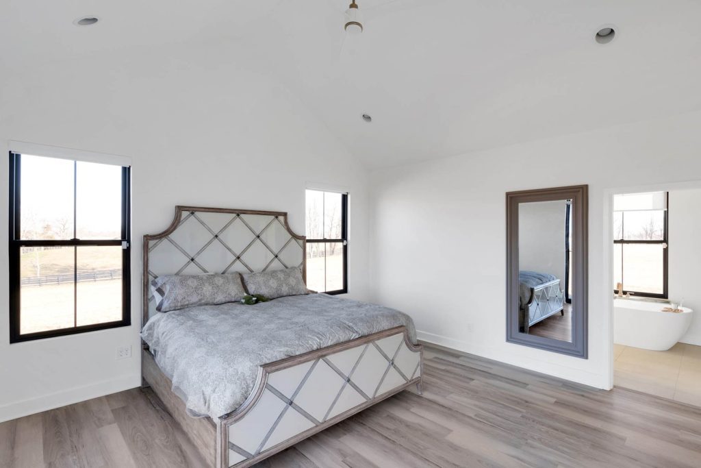 Louisville modern bedroom with patterned headboard, gray bedding, hardwood floors, and spacious, bright custom home design.