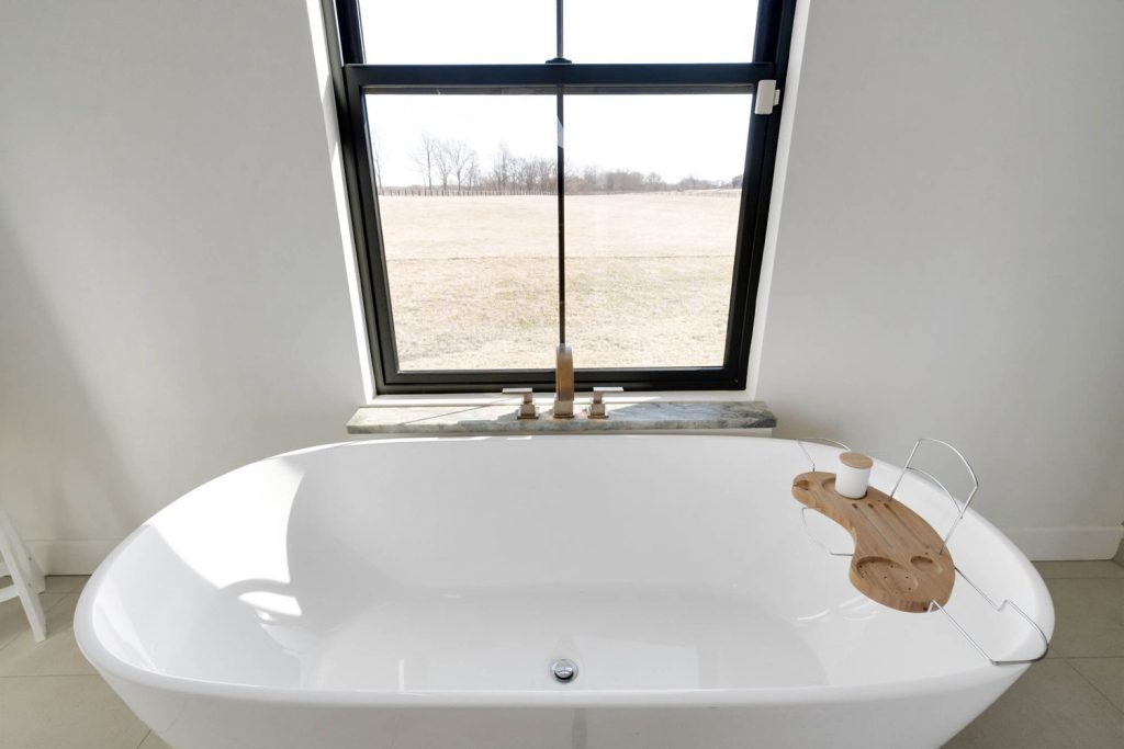 Louisville freestanding tub by large window with wooden tray, showcasing custom home design ideas in a serene spa-style bathroom.
