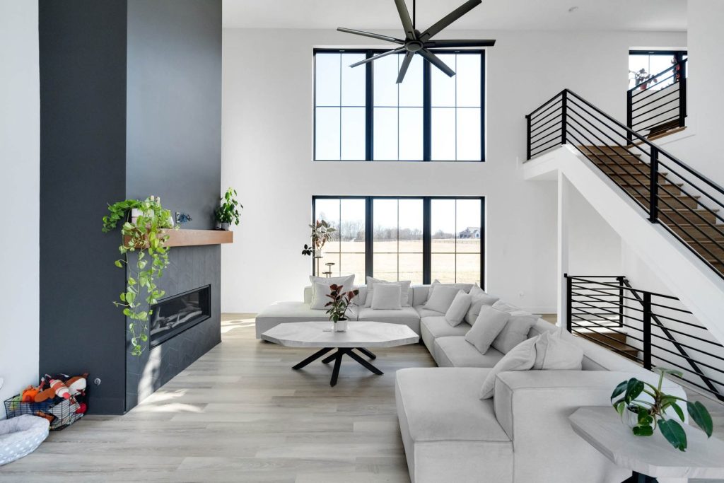 Louisville modern living room with tall windows, gray sectional, and sleek fireplace by top custom home builders.