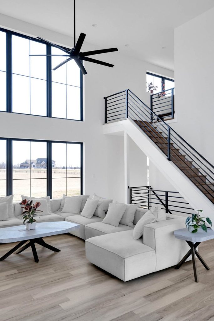 Louisville modern living room with white sectional, sleek staircase, and airy minimalist design by top custom home builders.