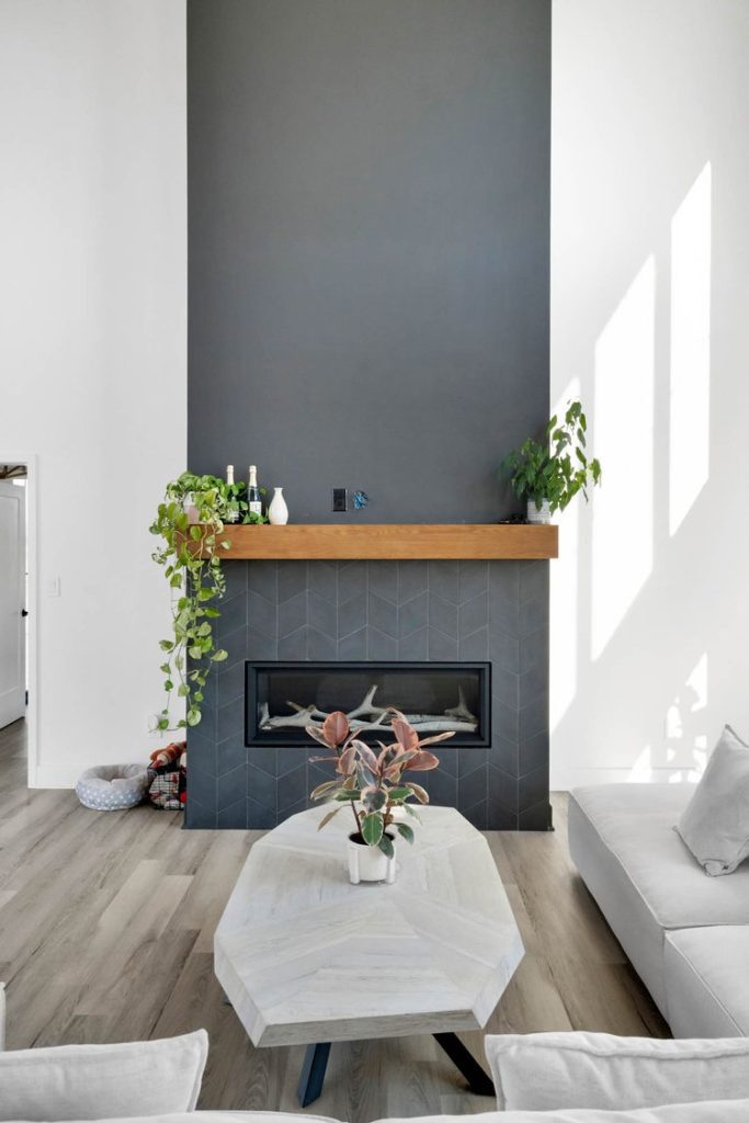 Louisville modern living room with black fireplace, wooden mantel, and greenery, designed by top custom home builders.