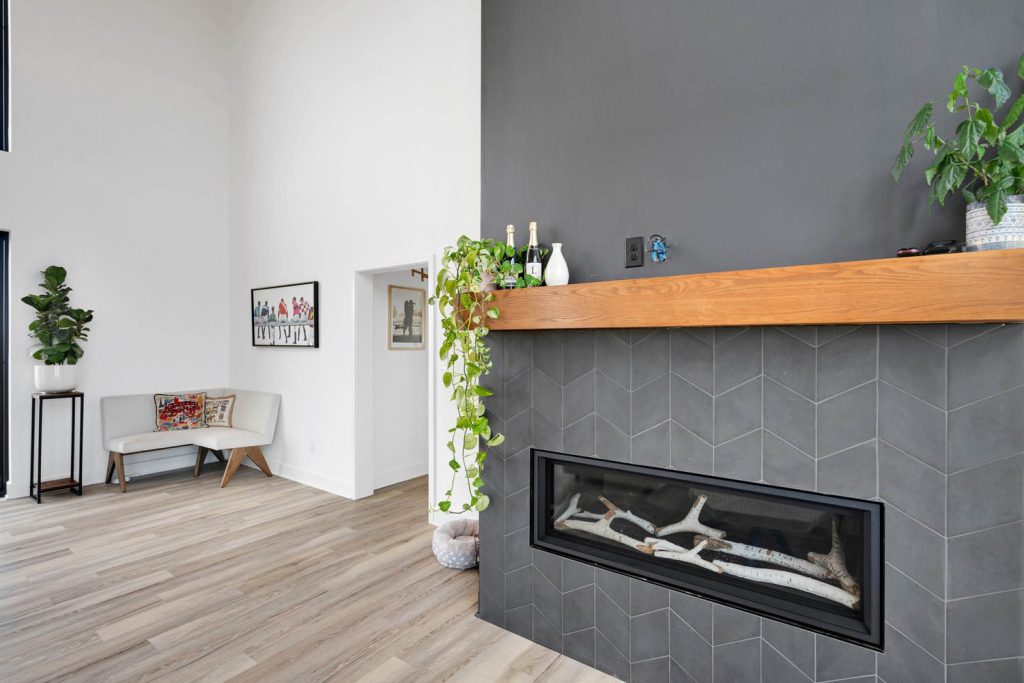 Modern Louisville living room with gray herringbone fireplace, wood mantel, cascading greenery, and light hardwood floors.