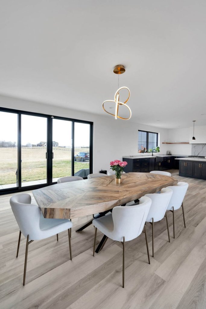 Louisville modern dining room with large wooden table, gray chairs, pink flowers, and field views through big windows.