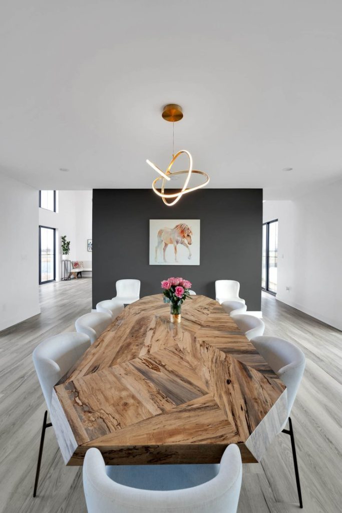 Louisville modern dining area with wooden geometric table, white chairs, pink flowers, black accent wall, and gold pendant light.