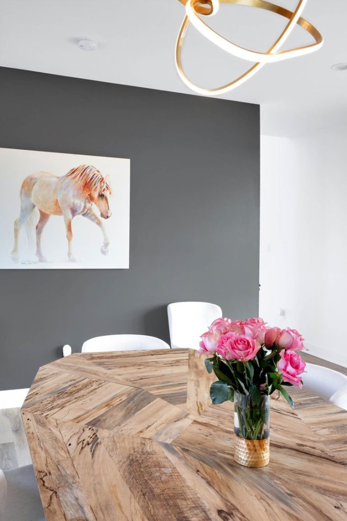 Louisville modern dining room with wooden table, pink roses, white chairs, and dark gray accent wall with artwork.