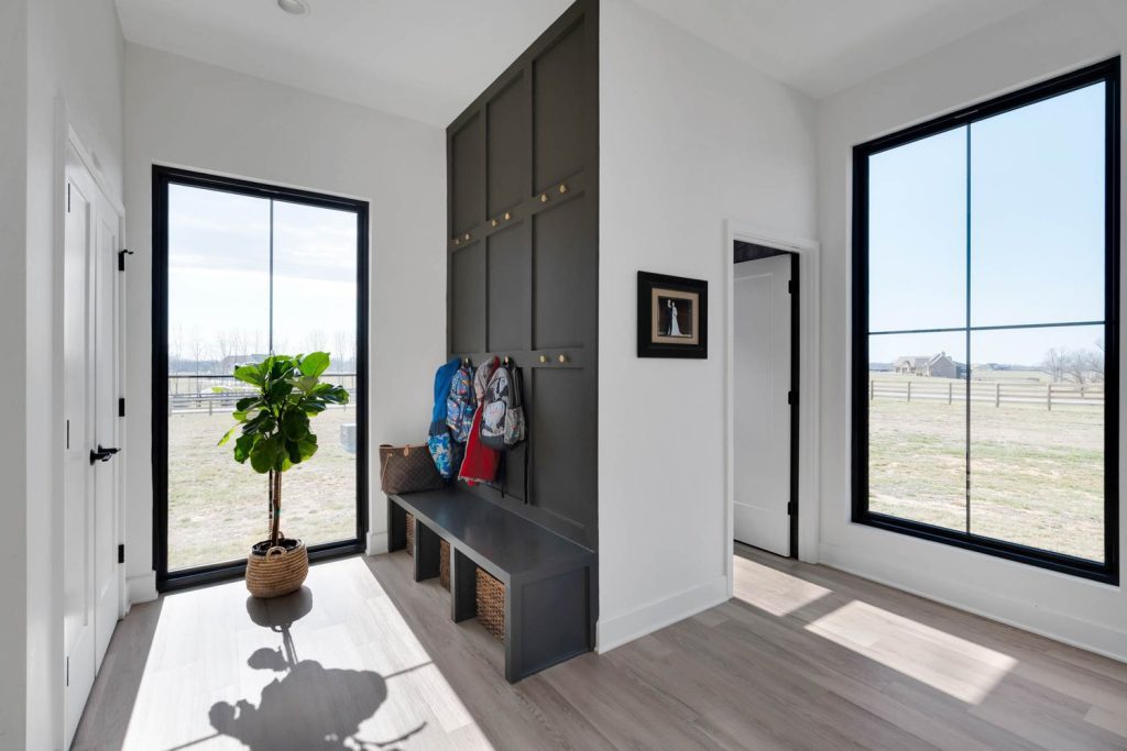 Louisville modern mudroom with dark built-in storage, bench with baskets, and backpacks hanging by large windows.
