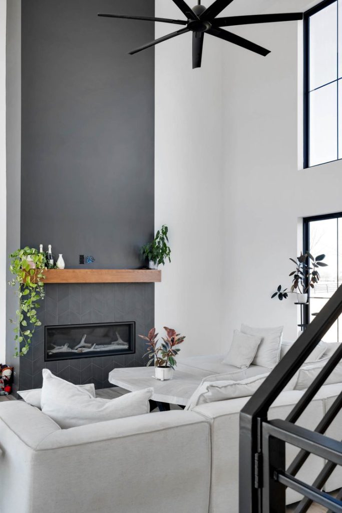 Louisville modern living room with tall gray fireplace, white sectional sofas, wooden mantel, greenery, and large windows.