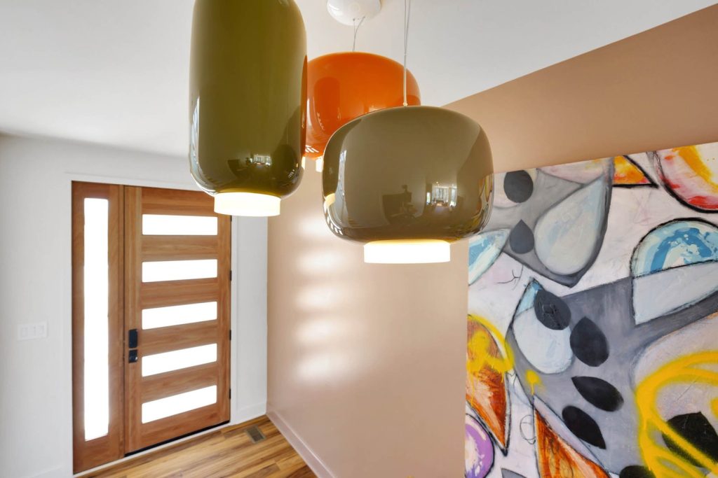 Three modern olive and orange pendant lights hang in a contemporary hallway with wood door and abstract art