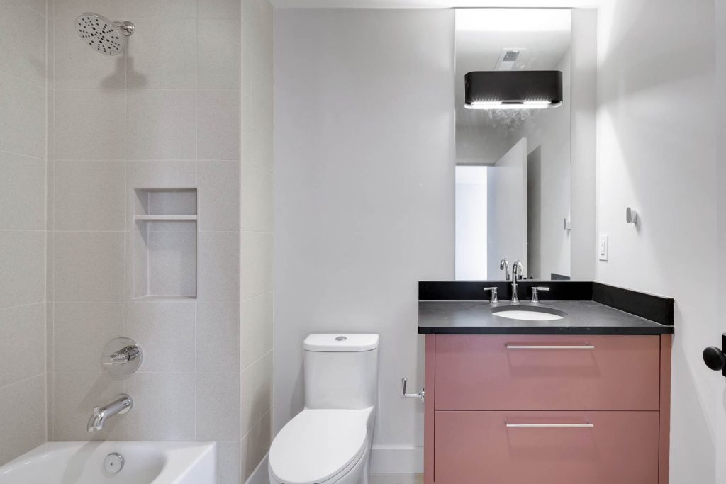 Modern bathroom with white toilet, pink vanity, and black countertop, showcasing new construction home design ideas by top custom home builders
