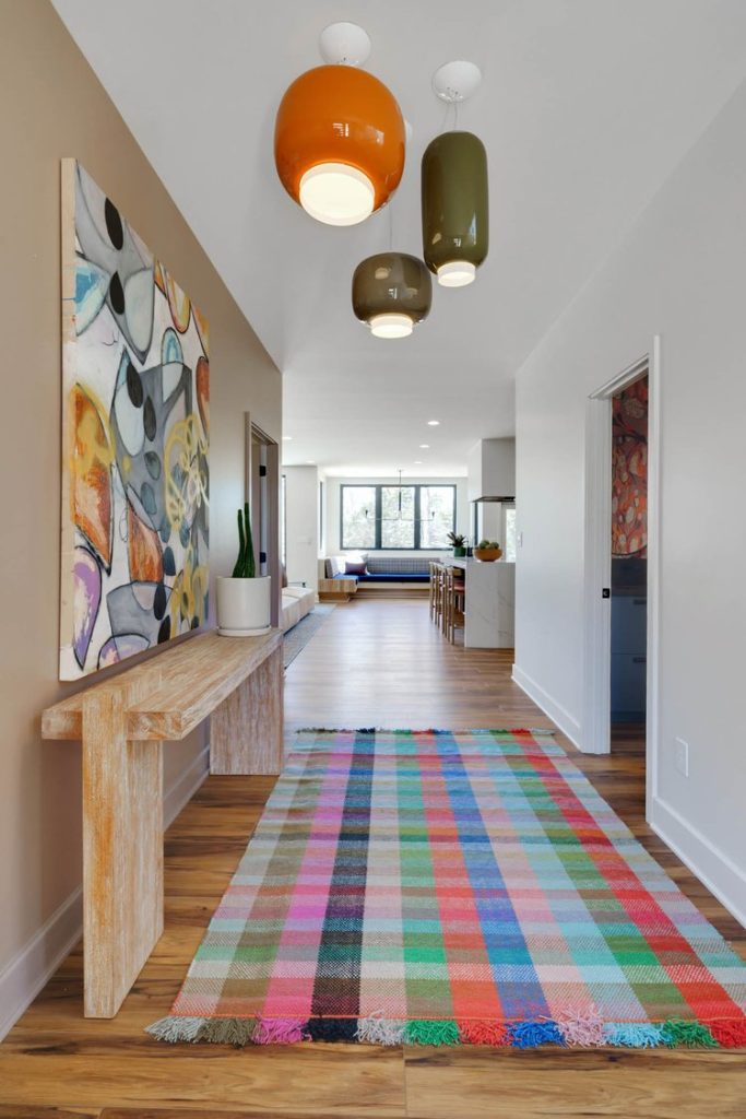 Modern hallway with wood floors, colorful abstract artwork, rustic console table with plants, and a vibrant checkered rug
