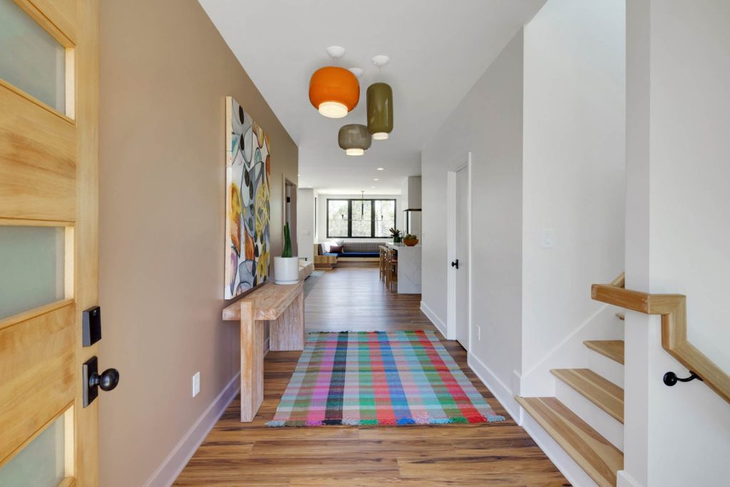 Modern hallway with colorful pendant lights, abstract wall art, wooden console table, plaid rug, and hardwood floors