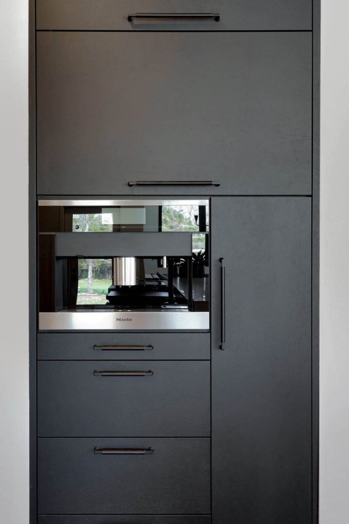 Modern kitchen with dark cabinets and built-in stainless steel coffee machine, featuring a minimalist and sophisticated design
