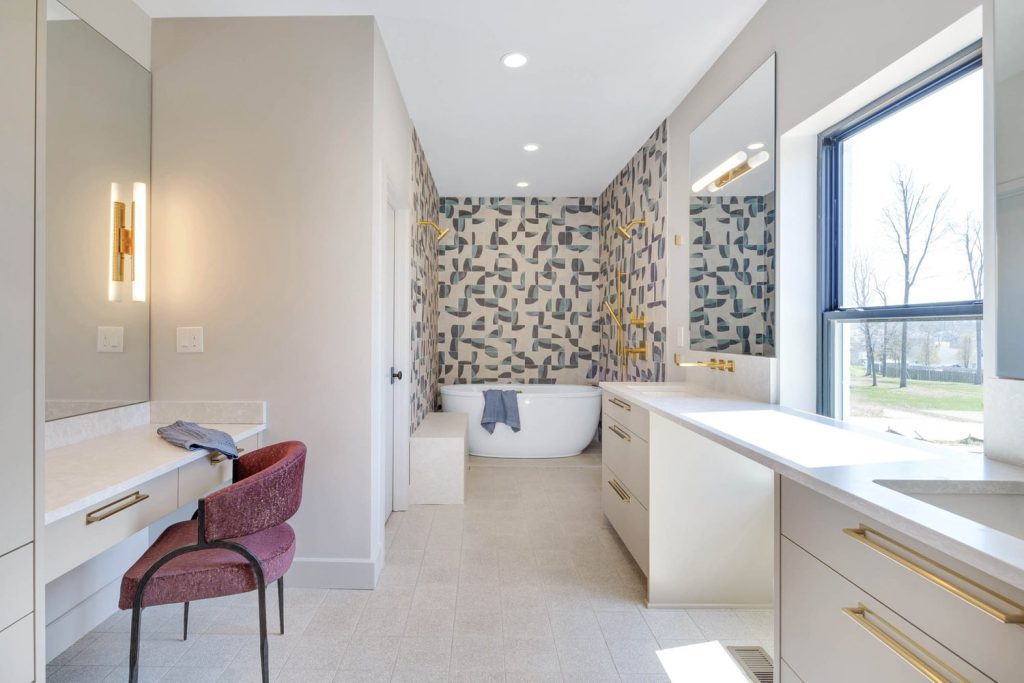 Modern bathroom with abstract accent wall, freestanding tub, double vanity, gold fixtures, and a large window