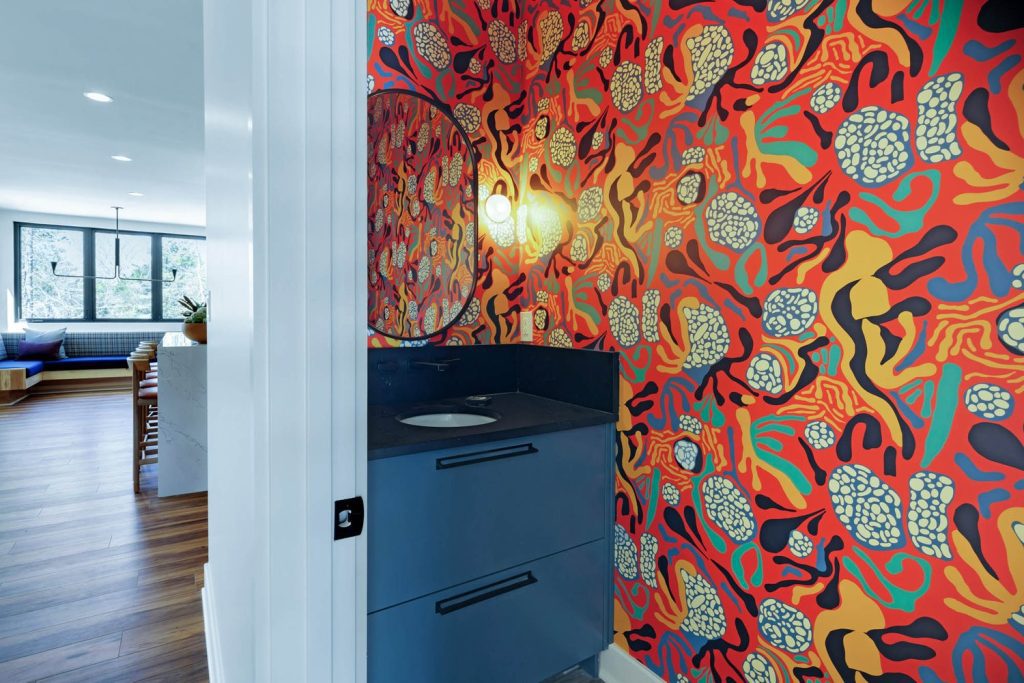 Vibrant bathroom with abstract wallpaper, round mirror, and sleek blue vanity, creating a modern, artistic atmosphere