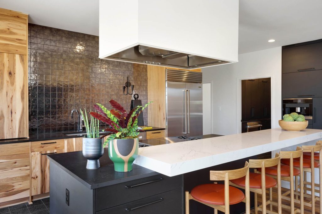 Modern kitchen with white island, stainless steel appliances, dark brown backsplash, and colorful plant vases