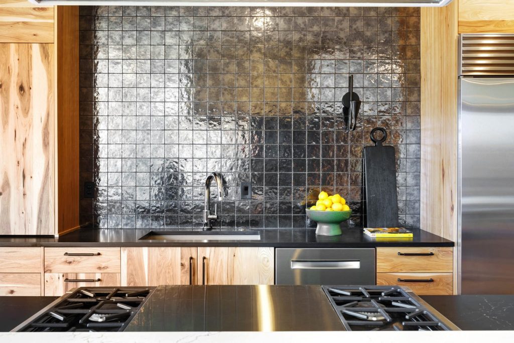 Modern kitchen with wooden cabinets, glossy tiled backsplash, stainless steel appliances, and lemons on the countertop