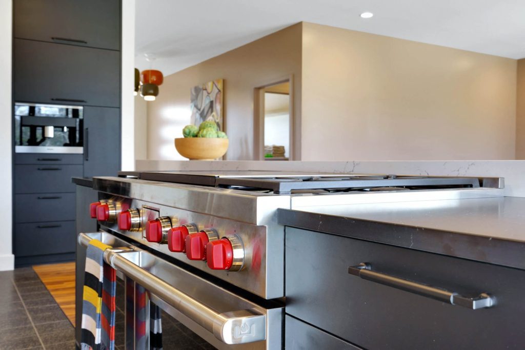 Modern kitchen with stainless steel stove with red knobs, wooden bowl of vegetables, and a bright, inviting atmosphere