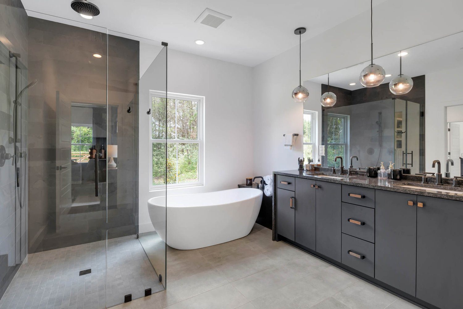 Bathroom with black vanity, pendant lights, large mirrors, walk-in shower, and freestanding tub by window in a minimalist style.